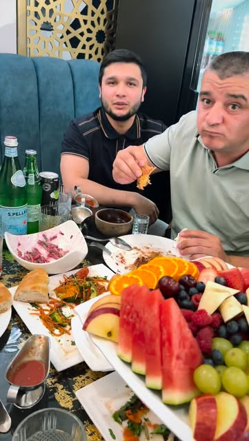 Guests at a table laid with a large fruit platter, salads and tea